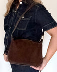 woman wearing a dark denim jacket holding a dark brown suede and leather crossbody/ shoulder bag