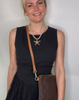 Woman wearing a black dress, holding a dark brown clutch / crossbody handbag.