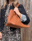 woman wearing a denim jacket and leopard print dress holding a dark tan woven handbag