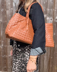 woman wearing a denim jacket and leopard print dress holding a dark tan woven handbag
