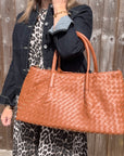 woman wearing a denim jacket and leopard print dress holding a dar tan woven handbag