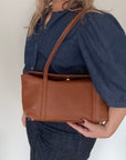 woman holding a dark tan leather shoulder handbag