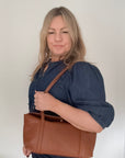 woman with blond hair and a denim shirt is holding a dark tan leather shoulder handbag