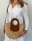 woman holding a straw handbag with a brown handle against a white background