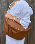Woman wearing a white dress, holding a brown leather handbag against a wooden fence background