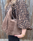 Lady wearing a leopard print top holding a taupe suede shoulder bag with leather trim