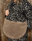 woman wearing a leopard print outfit holding a dark taupe suede crossbody/ shoulder bag