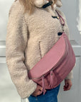 Woman wearing a beige fleece jacket with a pink crossbody bum handbag.
