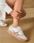 A person wearing white leopard print trainers with gold stars, paired with light-colored shorts.