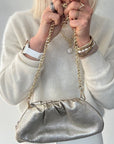 woman holding a silver handbag with gold chain strap against a plain background