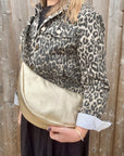 Woman wearing a leopard print jacket holding a gold crossbody handbag.