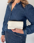 Woman wearing a blue denim shirt holding a gold clutch bag handbag with a gold accented chain.