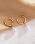 Gold hoop earrings with pearl drops on a beige fabric background