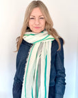 Woman wearing a green and white striped scarf over a denim shirt.