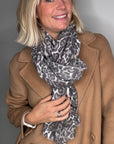 Woman wearing a tan coat and a grey animal print scarf