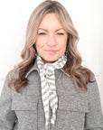 Woman wearing a grey coat and grey and cream patterned scarf against a white background