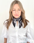 Woman wearing a white shirt and a grey animal print patterned scarf.