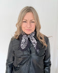 Woman wearing a black leather jacket with a grey animal print patterned scarf.