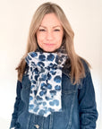 Woman wearing a blue and white animal print scarf with a denim jacket against a plain background