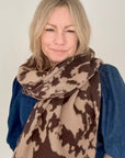 Woman wearing a large brown and beige cow print scarf on a plain background