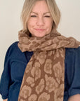 Woman wearing a camel & brown leopard print scarf on a plain background