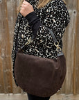 Person wearing a leopard print coat and holding a brown suede bag
