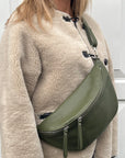 A woman wearing a khaki crossbody bum bag with silver accented hardware.