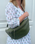 A woman wearing a khaki crossbody bum bag with silver accented hardware.