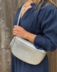 Woman wearing a navy dress, holding a silver crossbody bag against a wooden background.