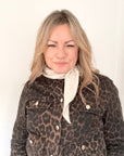 Woman wearing a leopard print jacket with a white scarf against a plain background