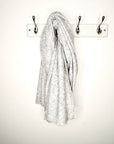 Grey knitted scarf hanging on a peg against a white wall