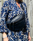 A person wearing a navy blue large crossbody bum bag with silver hardware and an adjustable strap.