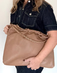 Woman holding a pale camel faux leather handbag with a gold chain strap against