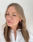 Woman wearing a white shirt and pink and orange beaded gold hoop earrings.