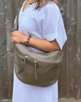Woman wearing a white dress, holding a dark taupe handbag against a wooden fence background.