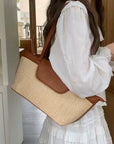 woman wearing a white dress holding a straw and dark tan summer handbag on her shoulder