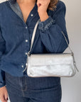 Woman wearing a blue denim shirt and holding a silver glittery clutch handbag.