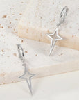 Silver star-shaped earrings on a textured beige surface