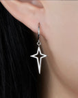 Silver star-shaped hoop earring worn by a person with dark hair.