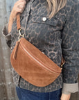 Woman wearing a leopard print jacket holding a dark tan suede bag against a wooden background.