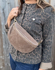 Woman wearing a leopard print jacket holding a dark taupe suede crossbody handbag.