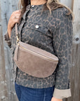 Woman wearing a leopard print jacket holding a dark taupe suede crossbody handbag.