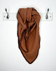 Brown and tan scarf draped over a white rack with hooks on a white background
