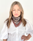 Woman wearing a white shirt and an animal print square scarf.
