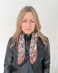 Woman wearing a black leather jacket and a animal print square scarf.