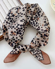 Animal print square scarf tied neatly on a white surface with a magazine in the background.