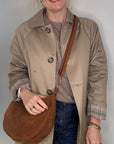 Woman wearing a beige trench coat holding a tan leather crossbody bag