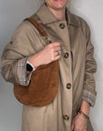 Woman wearing a beige trench coat holding a tan leather crossbody bag