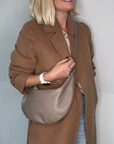 Woman wearing a brown coat holding a taupe crossbody/ shoulder handbag
