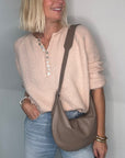 Woman wearing a beige sweater and blue jeans, holding a taupe crossbody/ shoulder bag